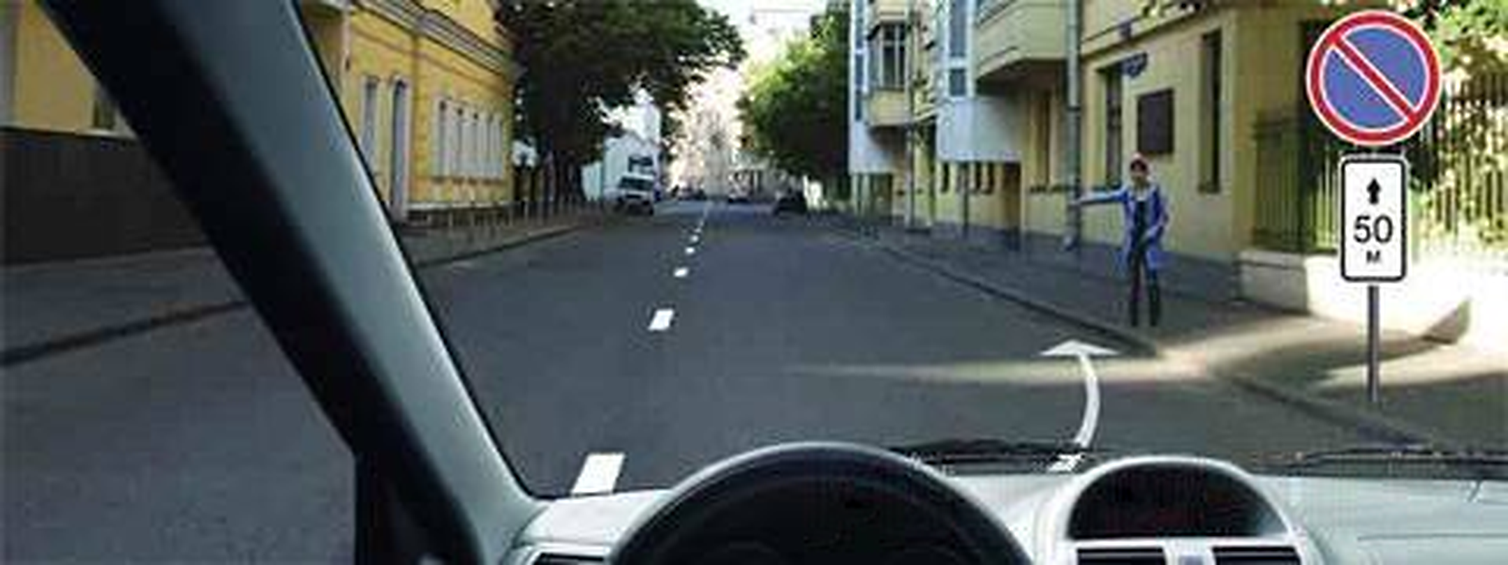 Street seen from a car; a blue circle with one red slash stands above a 50 m plate beside a curved white arrow.