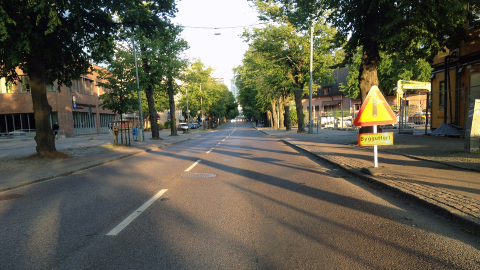 Urban street with a black-vertical-bar triangle and Byggutfart plate on the right.